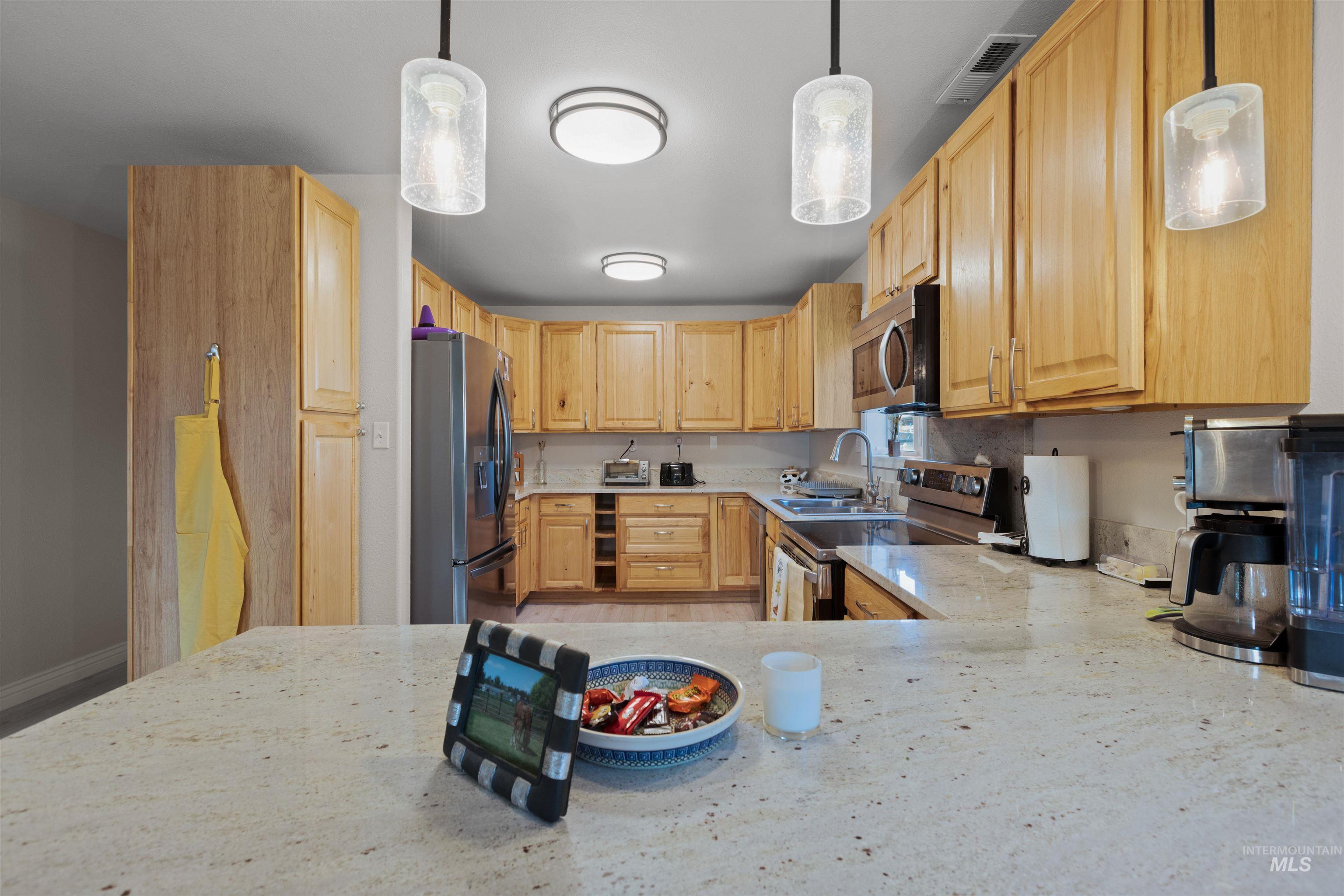 Kitchen featuring pendant lighting, light stone countertops, appliances with stainless steel finishes, and light brown cabinets