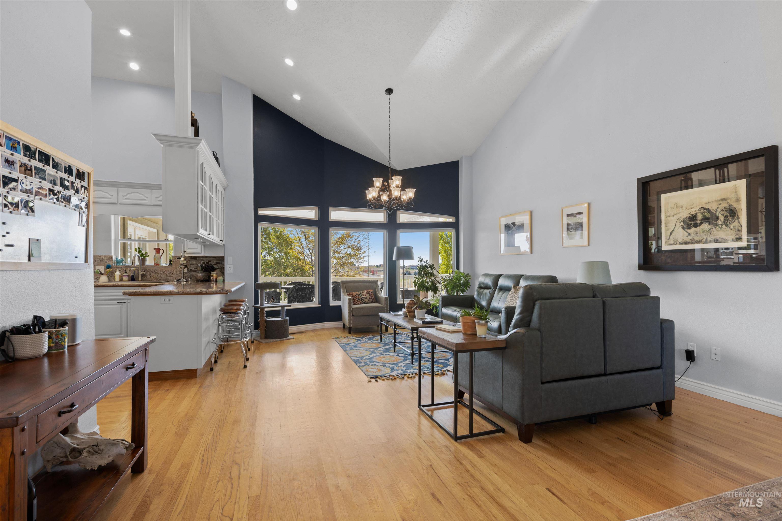 Living area with high vaulted ceiling, light wood finished floors, a chandelier, and recessed lighting