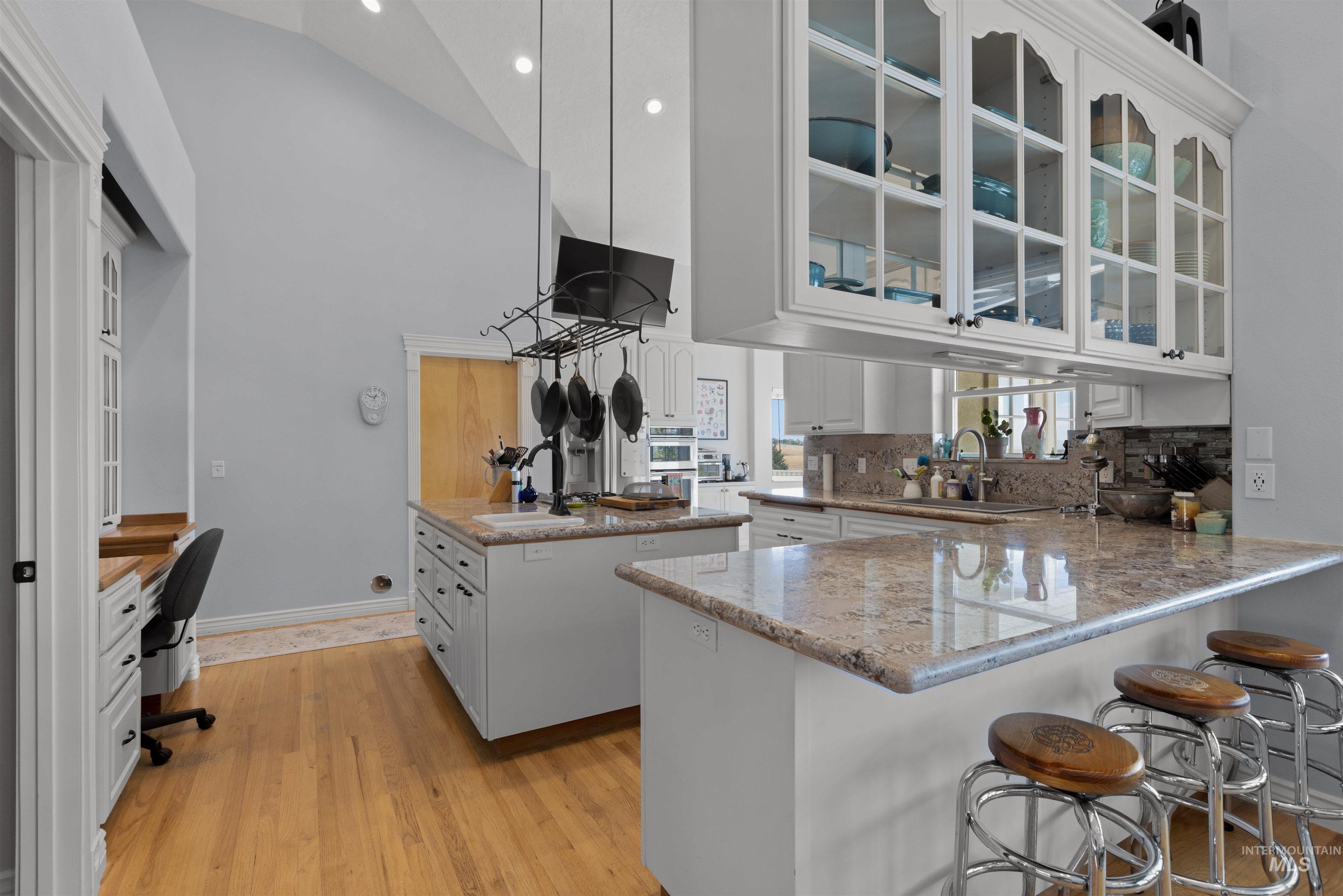 Kitchen with glass insert cabinets, white cabinets, light wood-type flooring, light stone countertops, and a kitchen breakfast bar