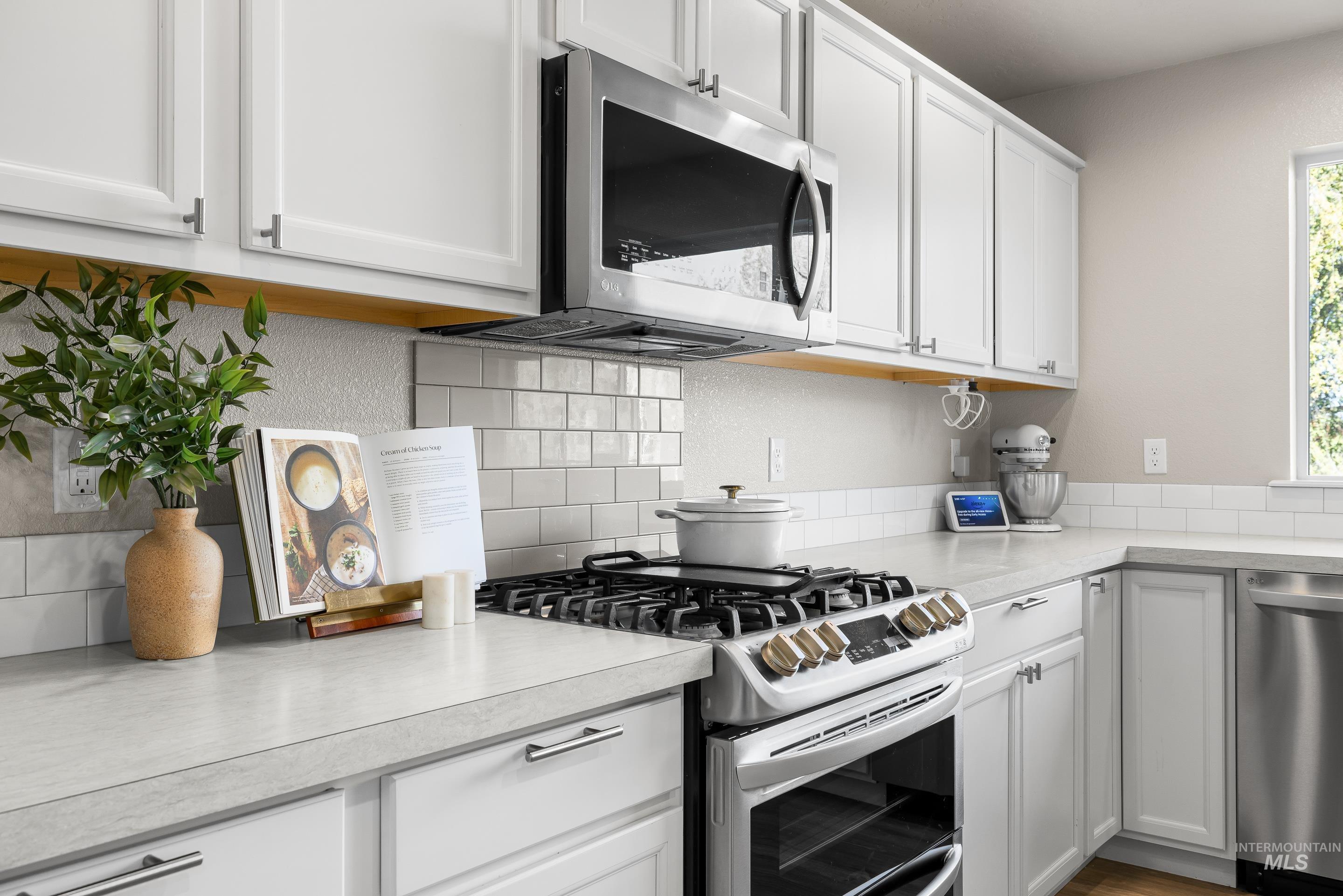 Kitchen with appliances with stainless steel finishes, light countertops, white cabinets, and tasteful backsplash