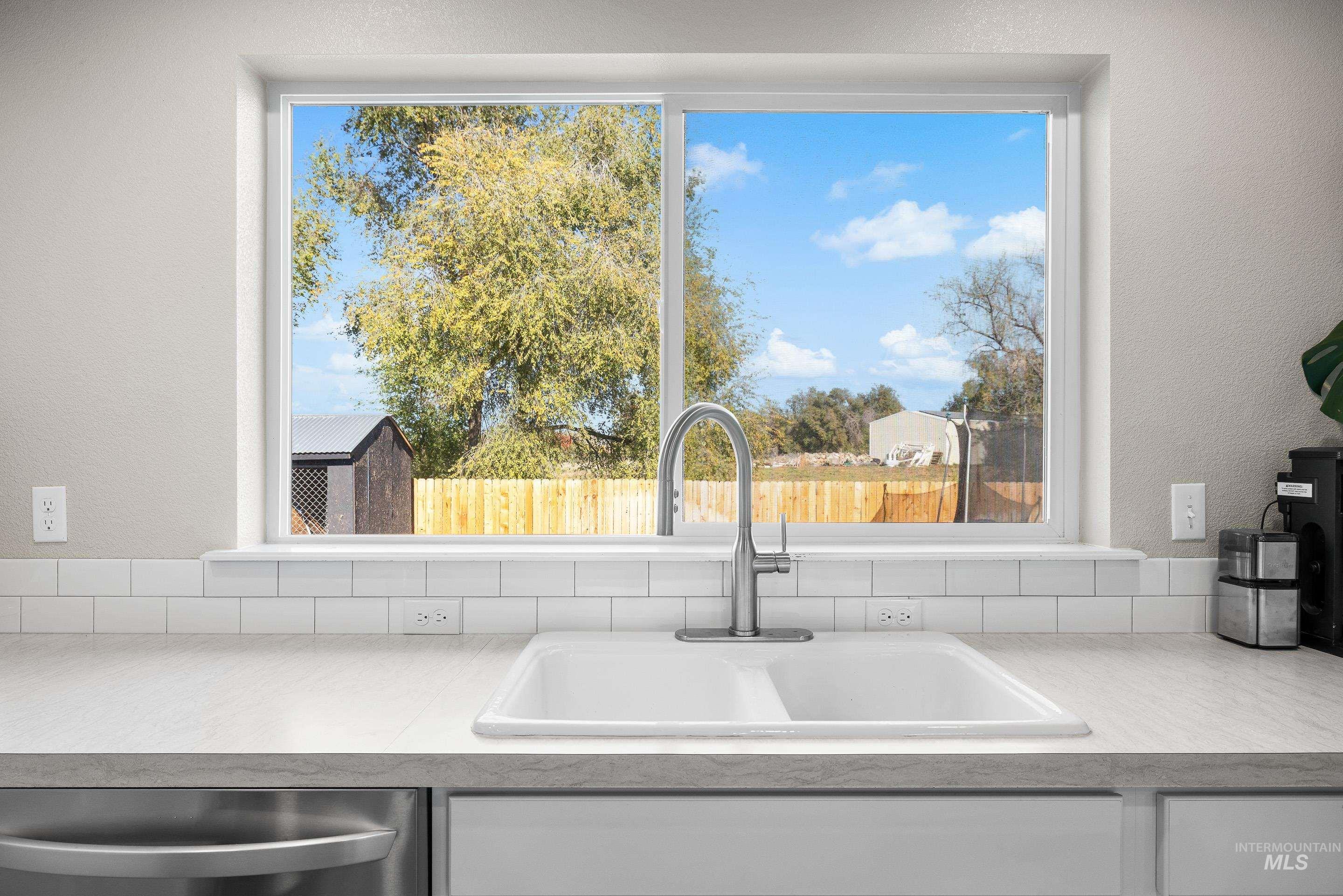 Kitchen view of a textured wall, light countertops, white cabinetry, and dishwasher
