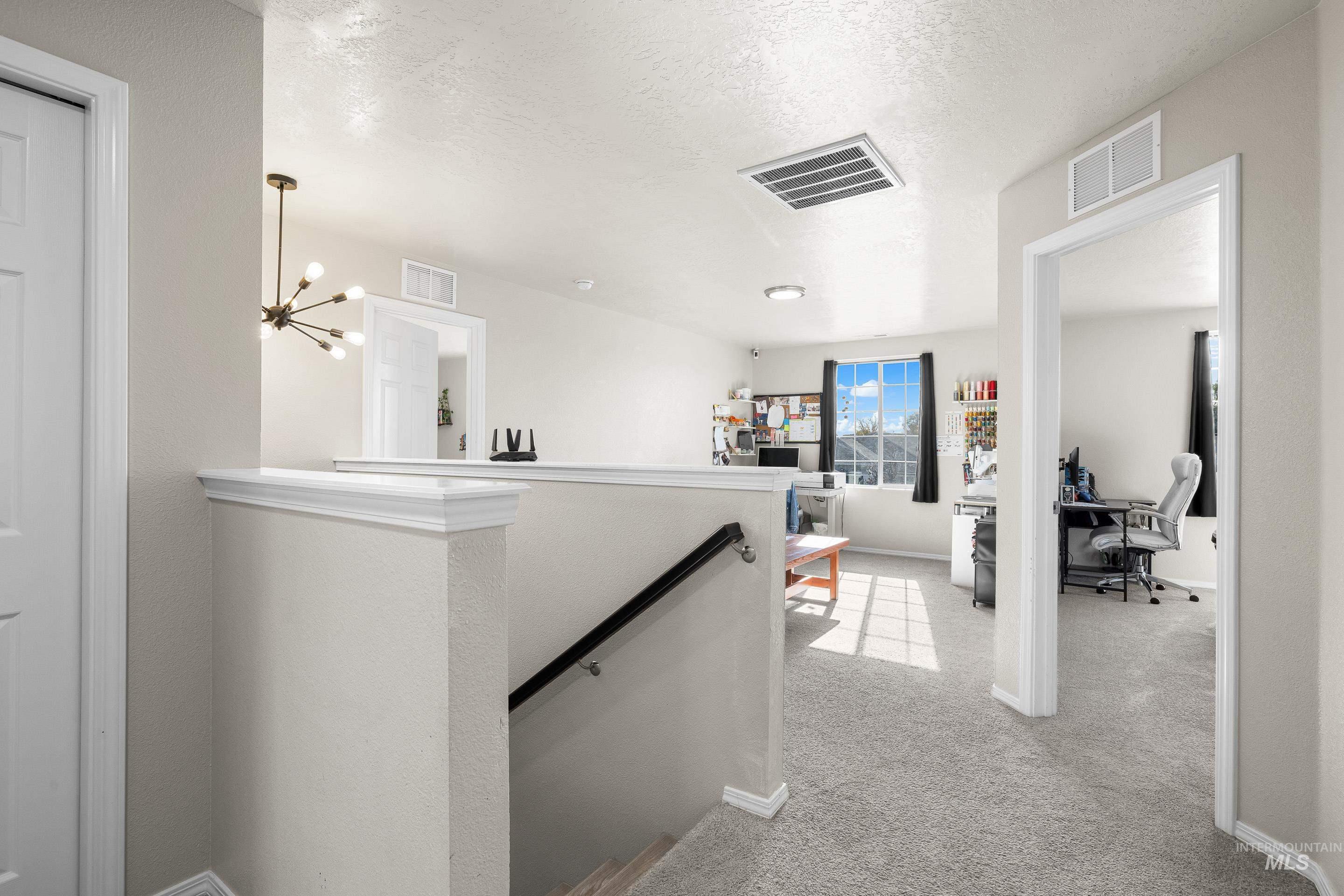 Hallway with an upstairs landing, an office area, light carpet, a textured ceiling, and a chandelier