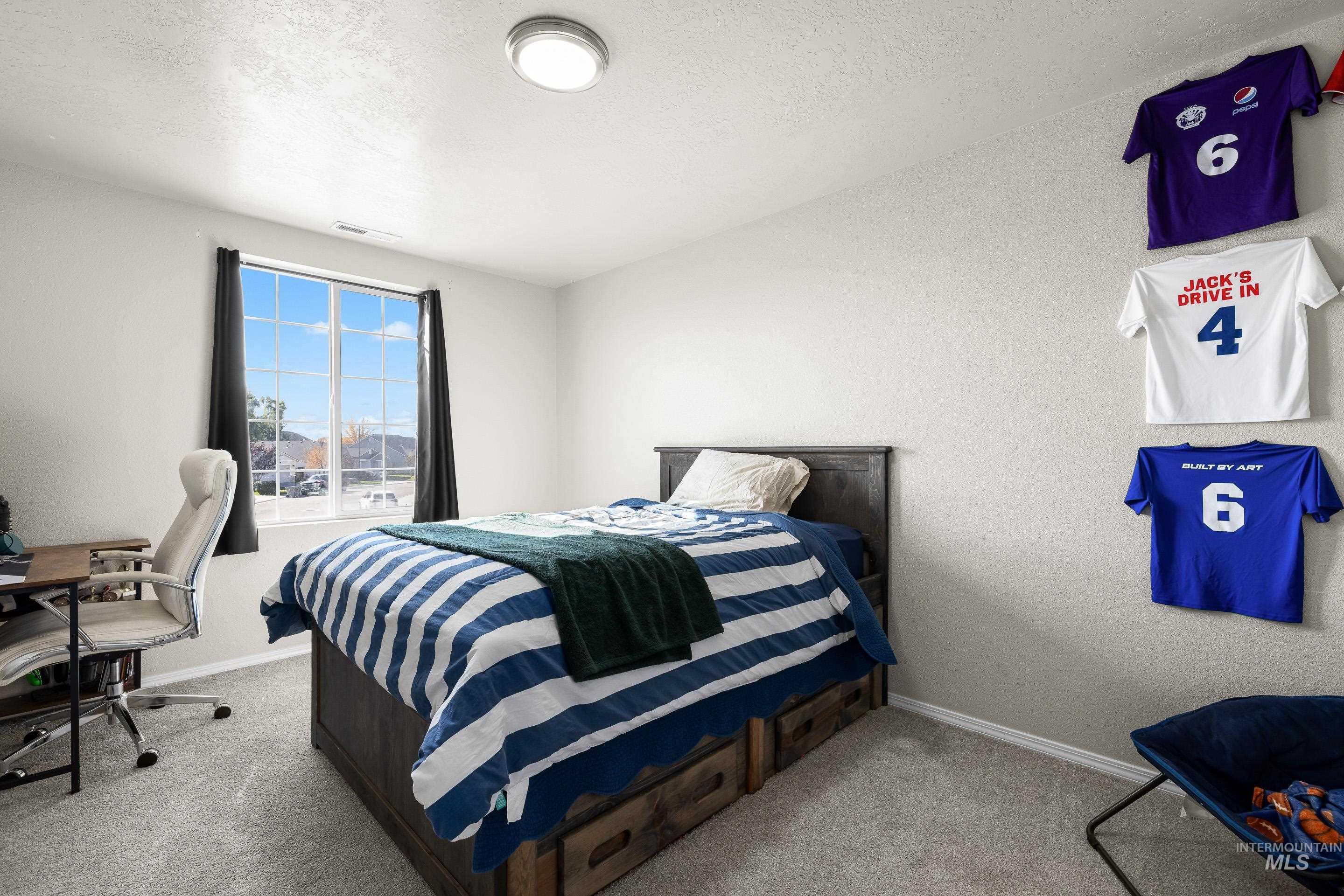 Bedroom featuring a textured ceiling, an office area, light carpet, and a textured wall