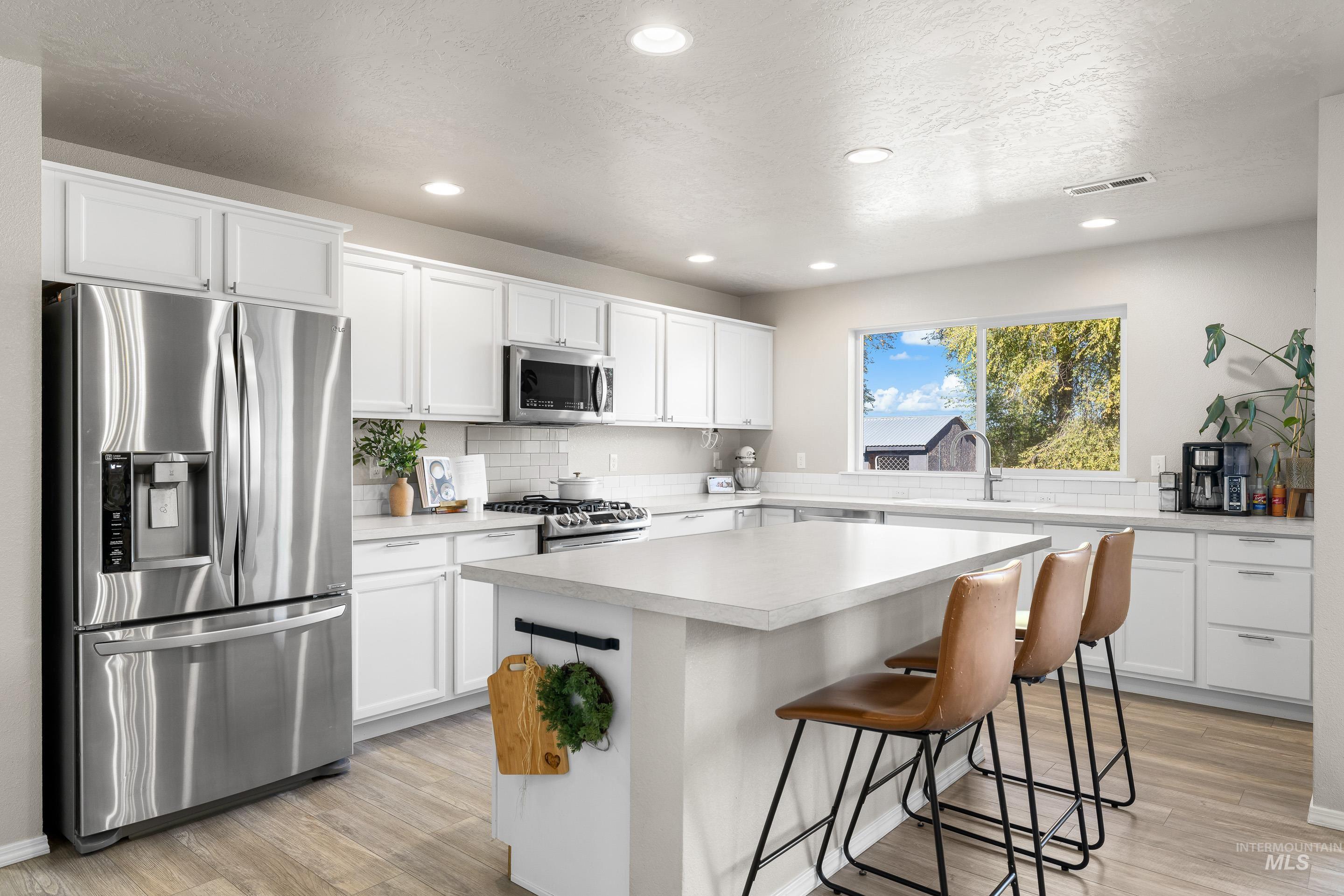 Kitchen with appliances with stainless steel finishes, light countertops, a kitchen bar, white cabinetry, and recessed lighting