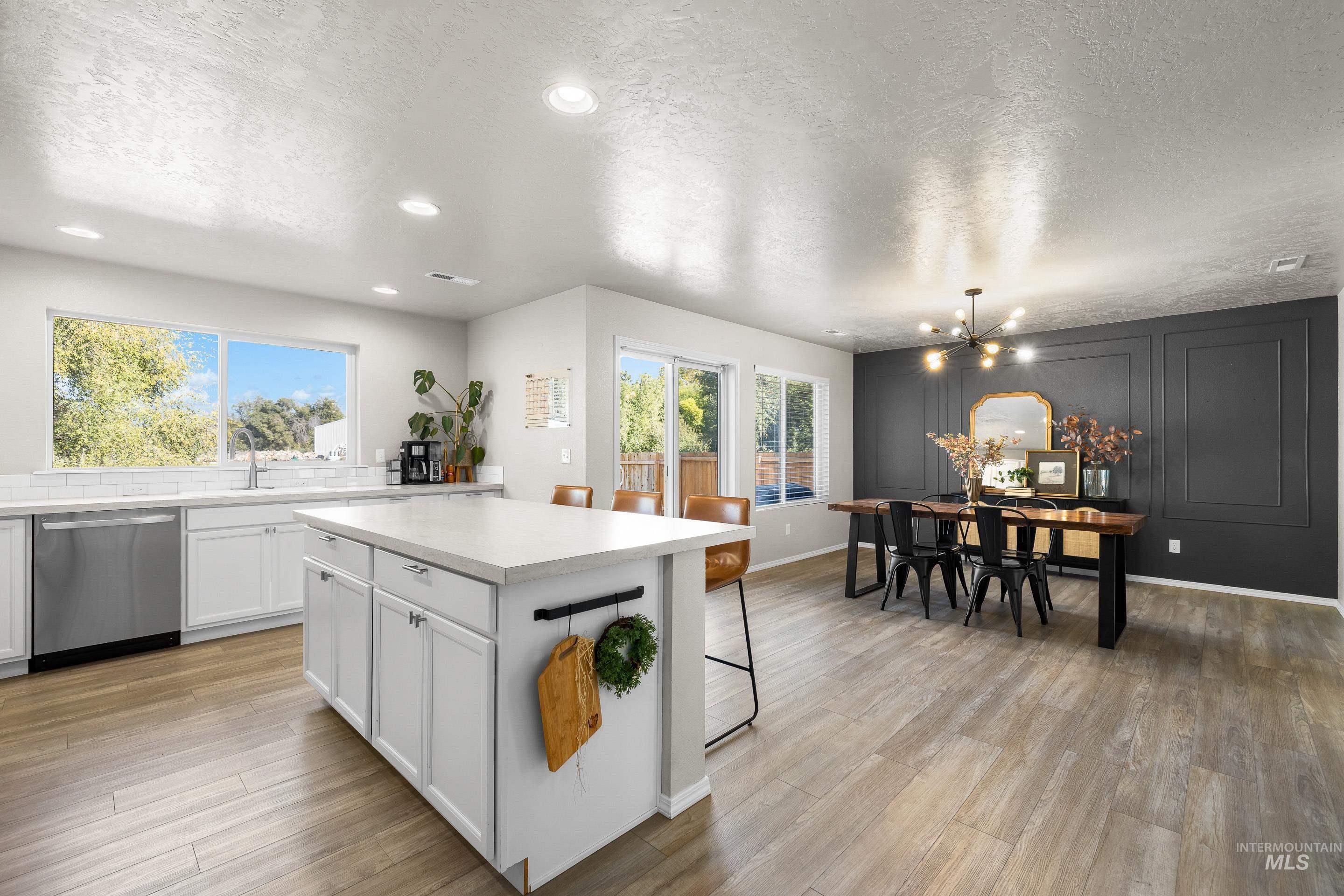 Kitchen featuring a textured ceiling, white cabinetry, light countertops, dishwasher, and a center island