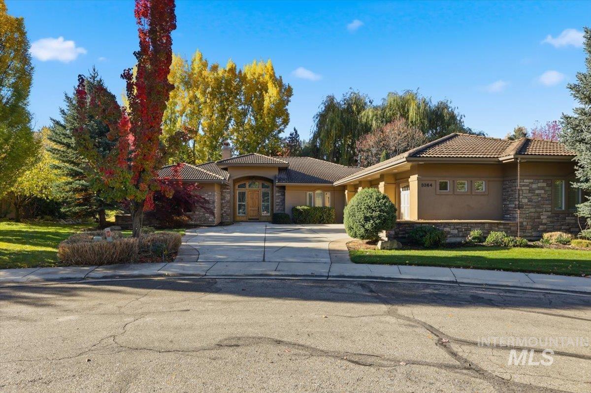 View of front of home with stone siding, driveway, stucco siding, and a tile roof