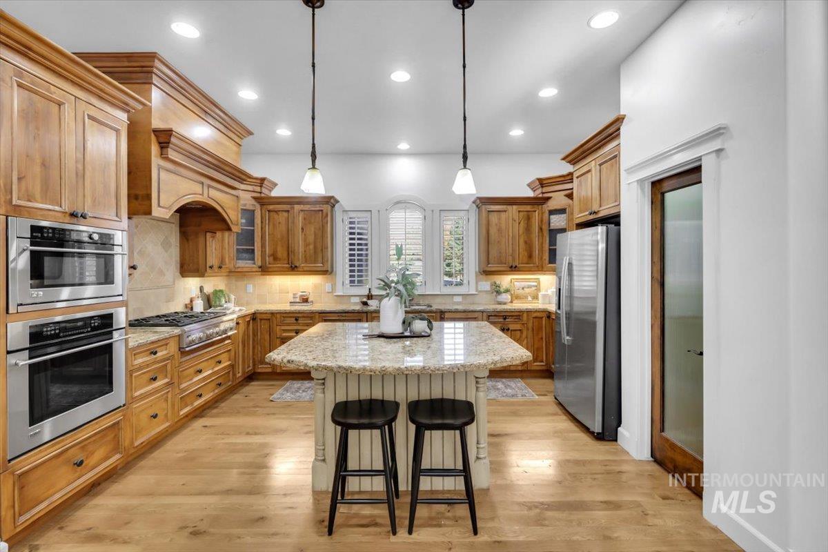 Kitchen with decorative backsplash, brown cabinetry, a breakfast bar area, light stone countertops, and light wood finished floors