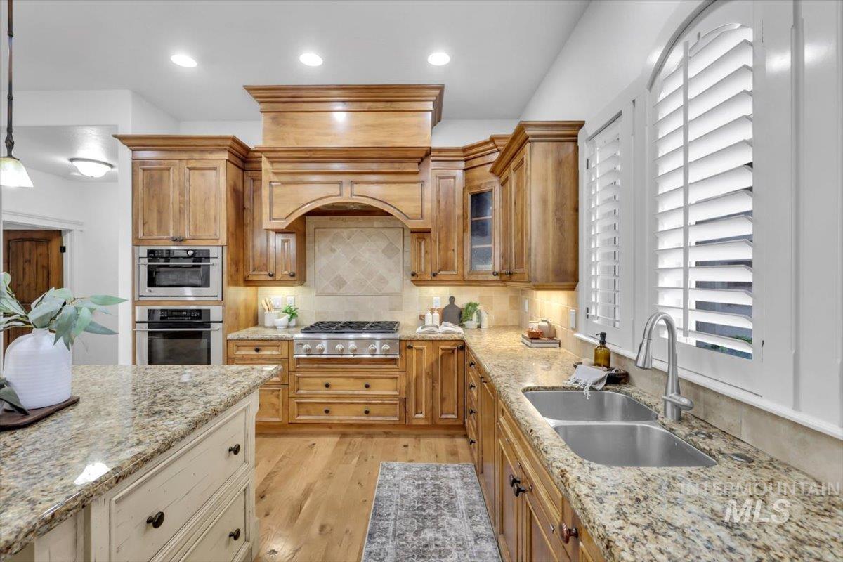 Kitchen featuring decorative backsplash, light wood-type flooring, light stone countertops, glass insert cabinets, and decorative light fixtures