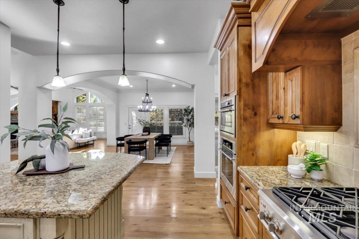 Kitchen featuring light stone counters, light wood-style flooring, decorative light fixtures, appliances with stainless steel finishes, and a chandelier