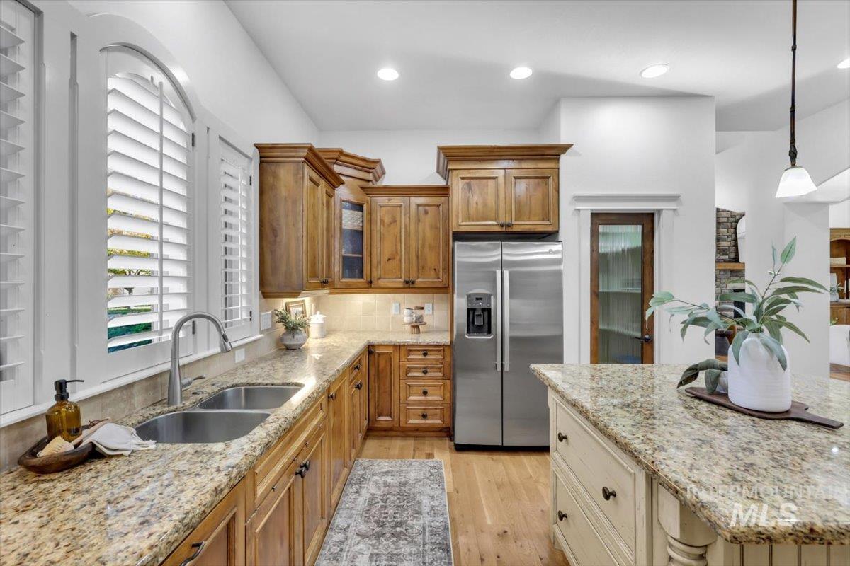 Kitchen with light stone countertops, stainless steel fridge with ice dispenser, brown cabinetry, light wood finished floors, and recessed lighting