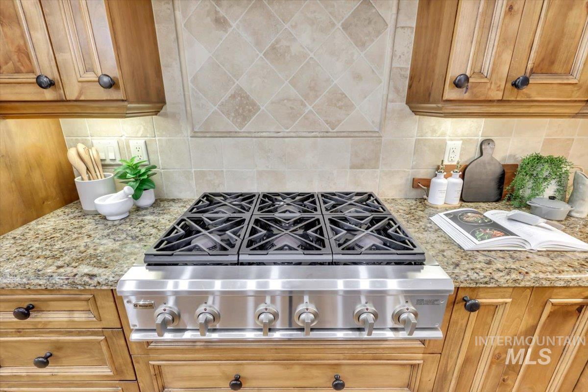 Kitchen with stainless steel gas stovetop, light stone counters, brown cabinets, and backsplash