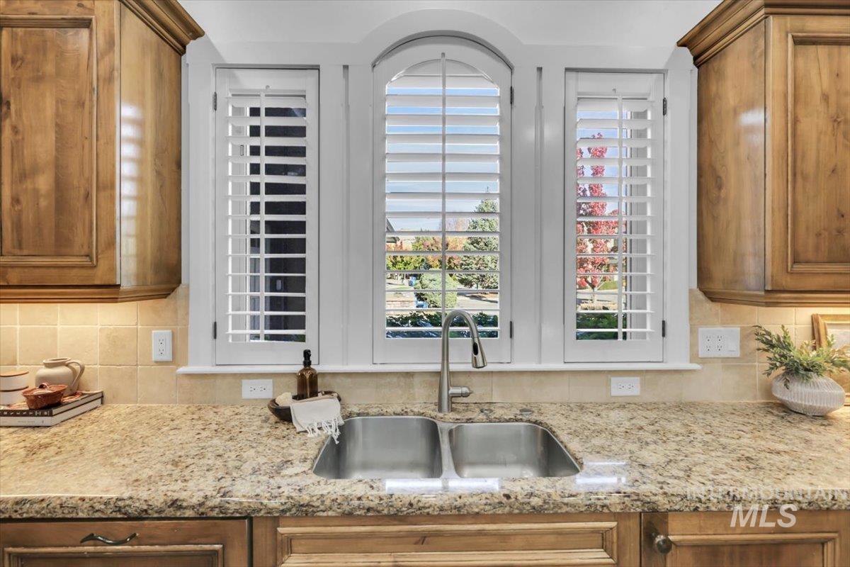 Kitchen featuring decorative backsplash, light stone counters, and brown cabinets