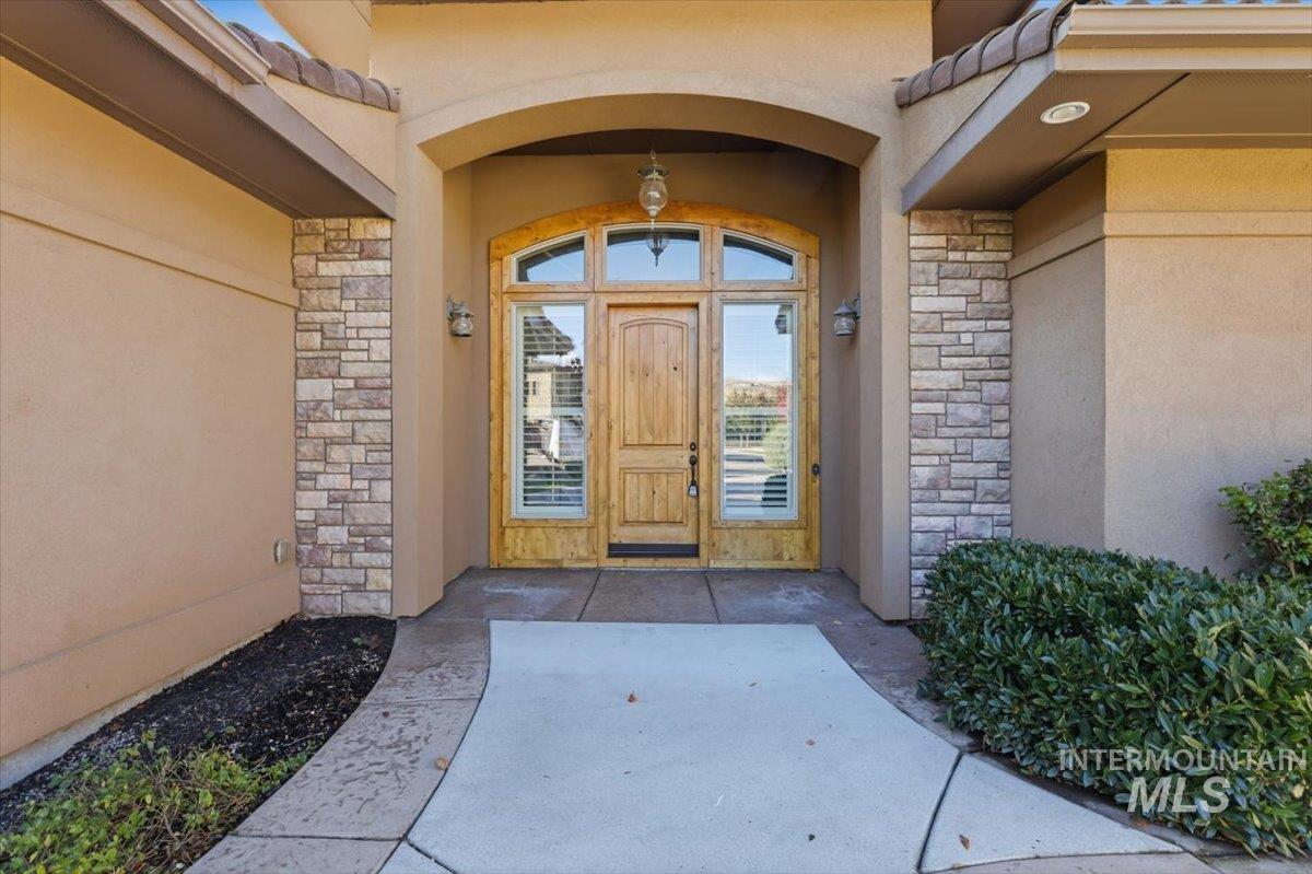 Doorway to property featuring stone siding, stucco siding, and a tile roof