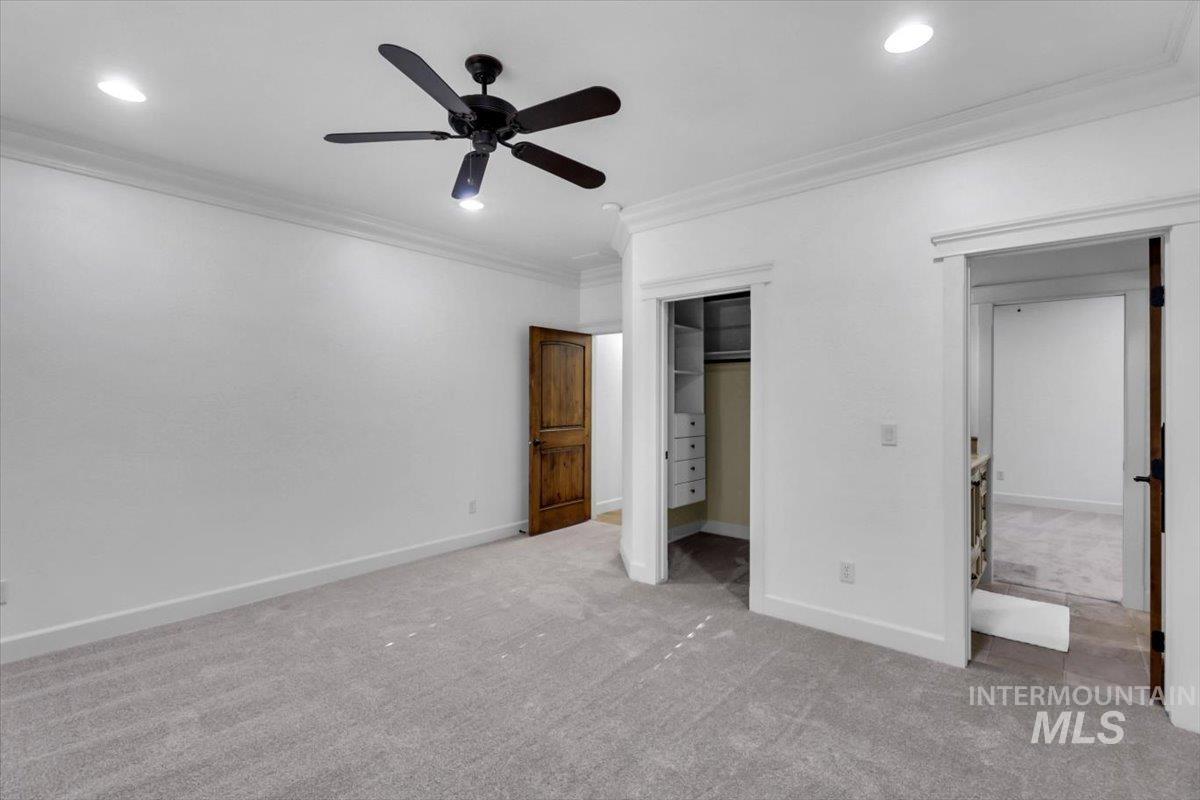 Unfurnished bedroom with crown molding, carpet floors, a walk in closet, a ceiling fan, and recessed lighting