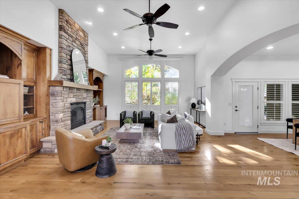 Living area with light wood-type flooring, recessed lighting, a stone fireplace, arched walkways, and a ceiling fan