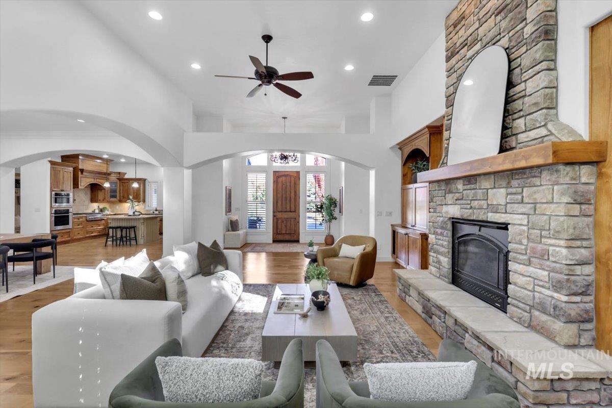 Living room featuring recessed lighting, arched walkways, light wood-style flooring, a ceiling fan, and a fireplace