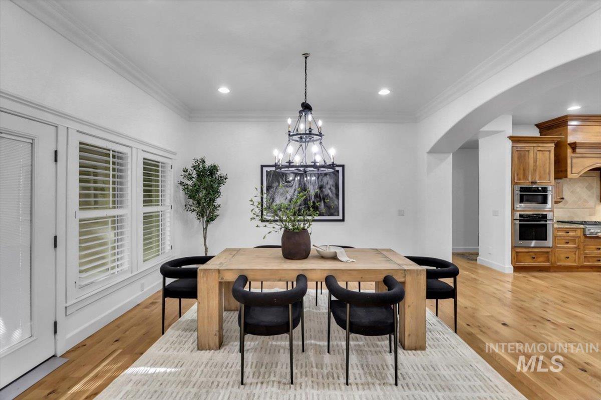 Dining space with crown molding, light wood-type flooring, a chandelier, arched walkways, and recessed lighting