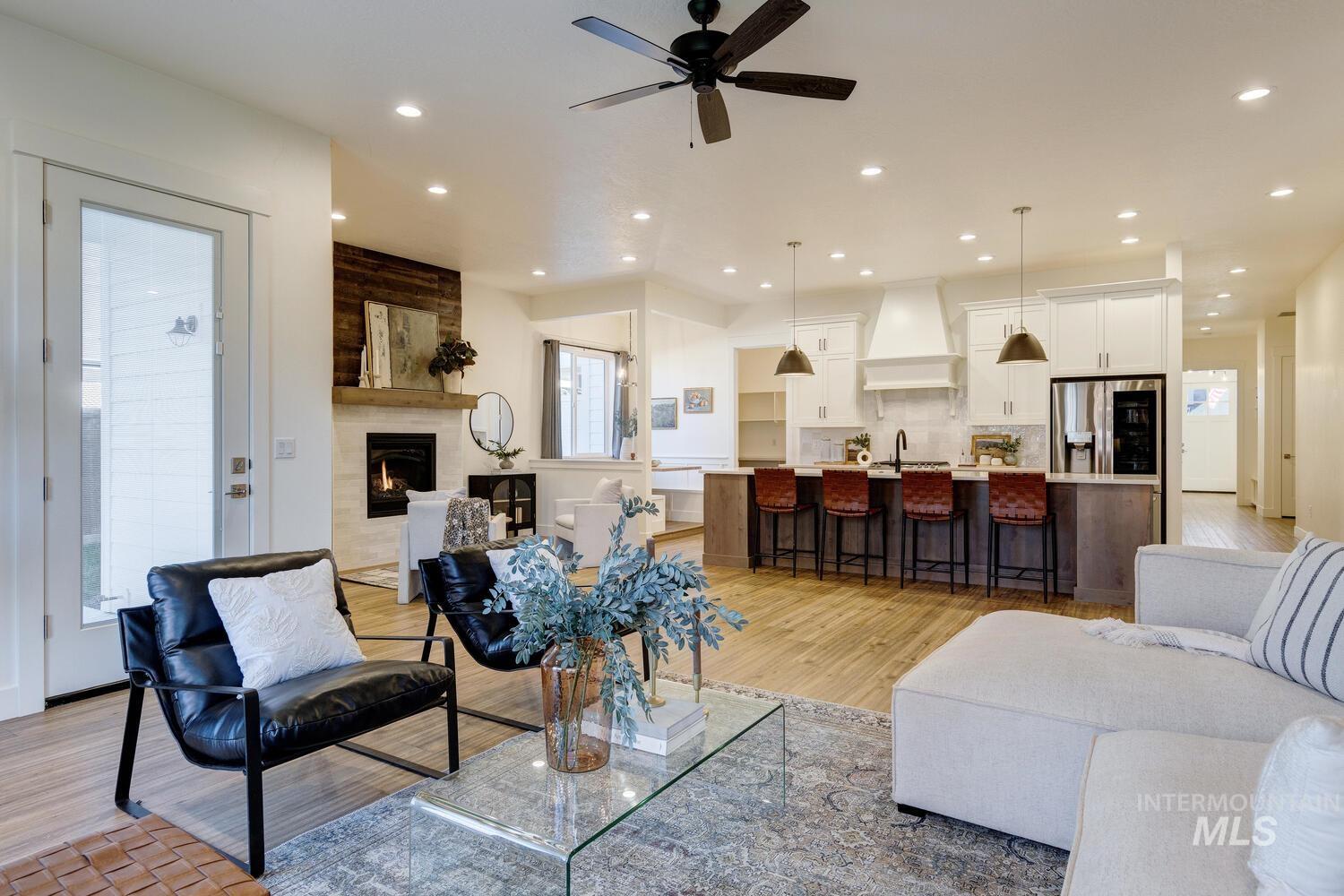 Living room with light wood-style flooring, plenty of natural light, a tiled fireplace, a ceiling fan, and recessed lighting