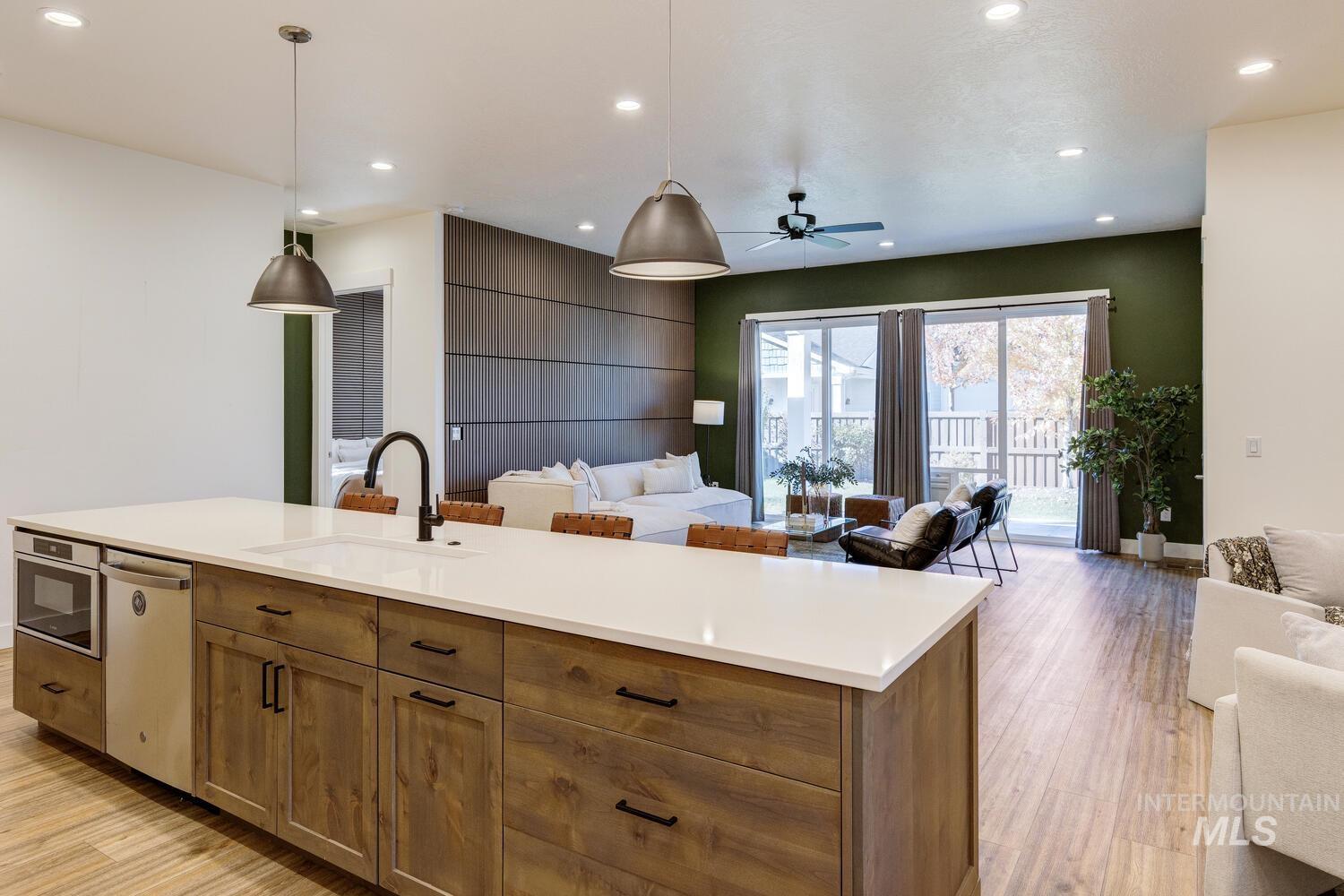 Kitchen with open floor plan, brown cabinetry, pendant lighting, an island with sink, and a ceiling fan