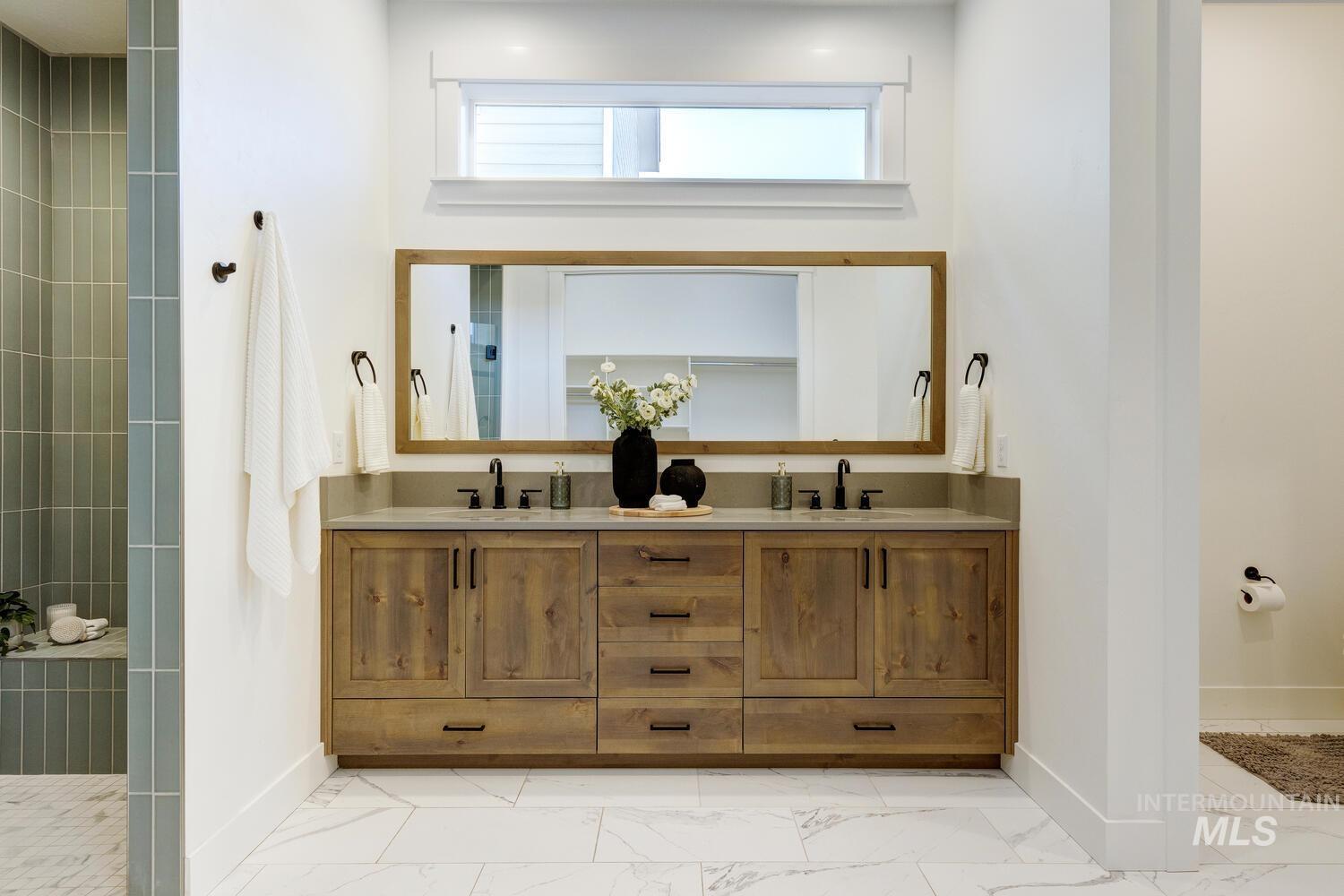 Bathroom with double vanity, light marble finish floors, and a tile shower