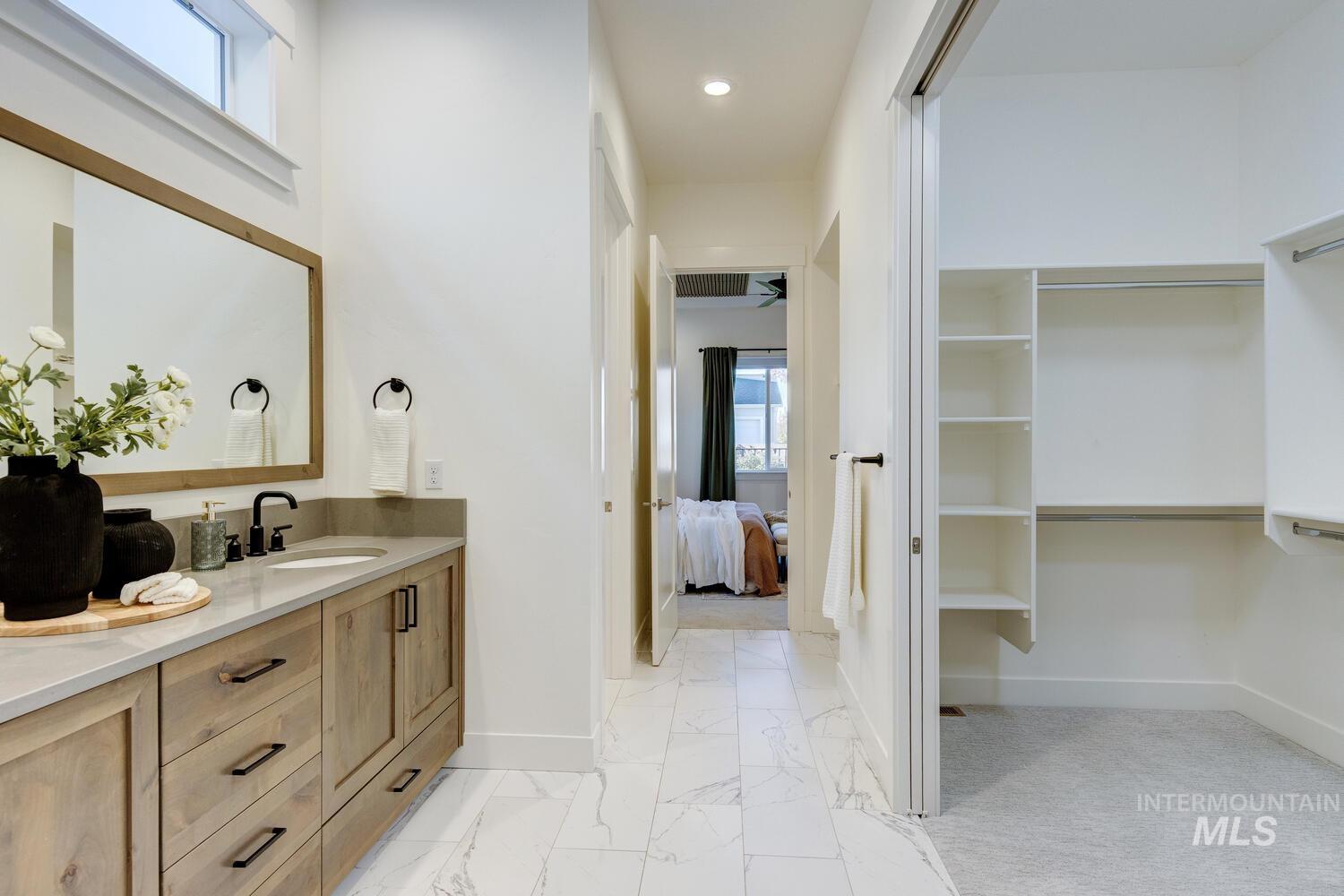 Ensuite bathroom with double vanity, light marble finish flooring, a spacious closet, and recessed lighting