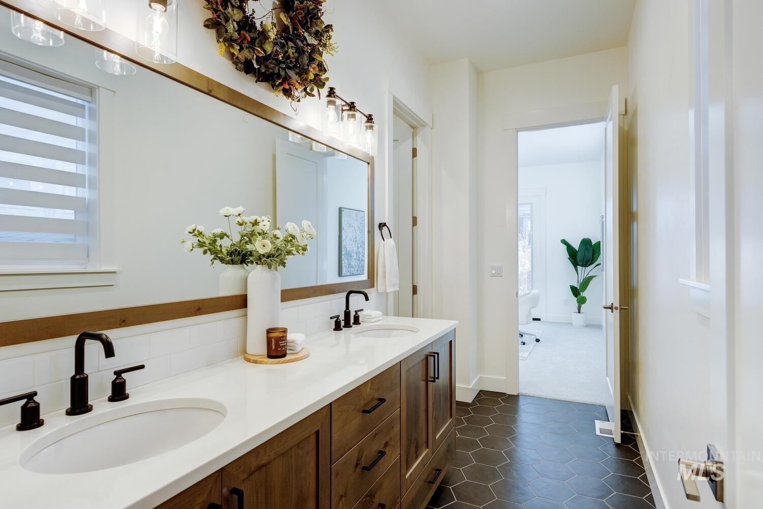 Full bathroom featuring double vanity, dark tile patterned flooring, and decorative backsplash