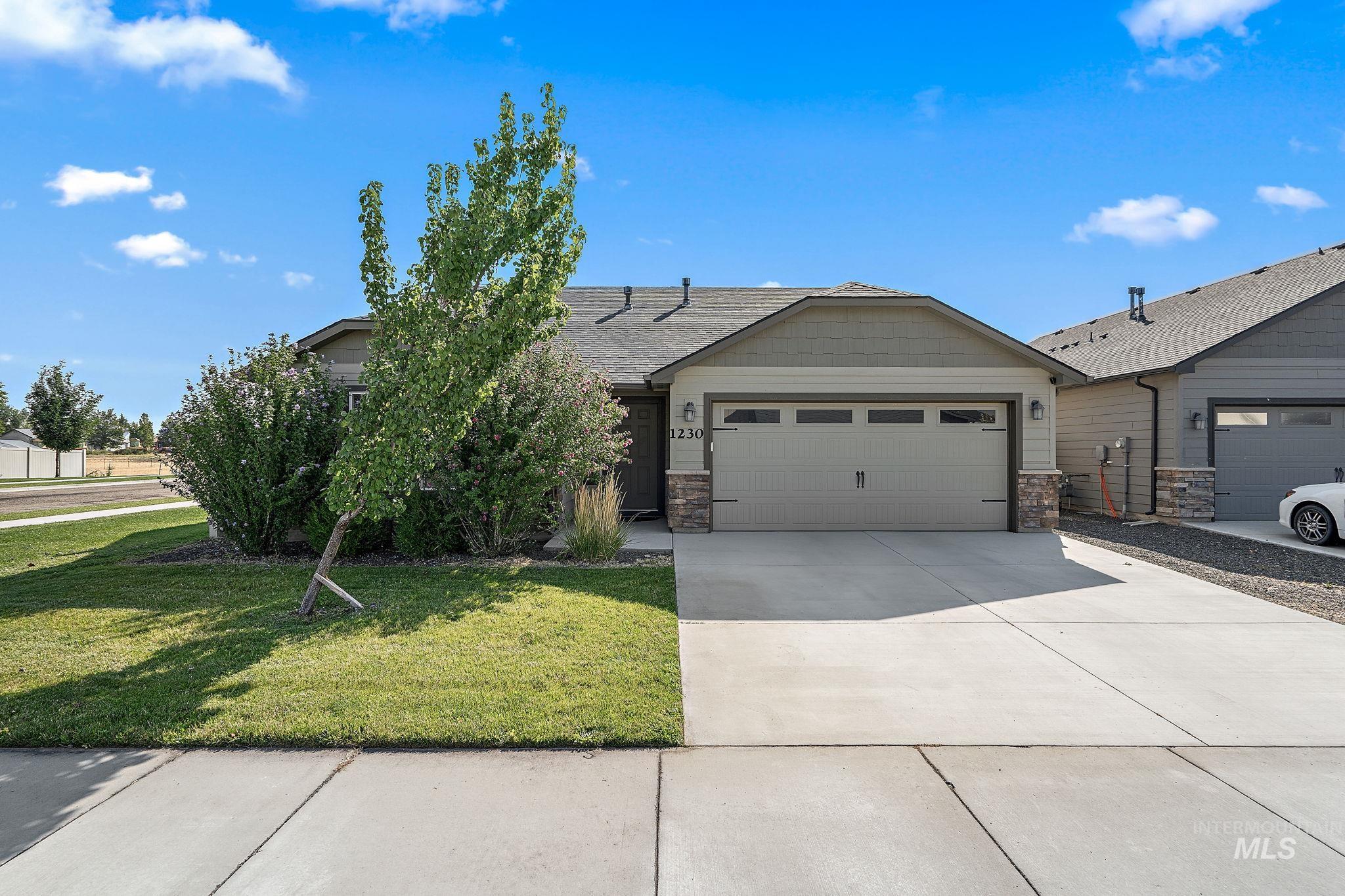 View of front of property featuring a garage, concrete driveway, stone siding, a front yard, and a shingled roof