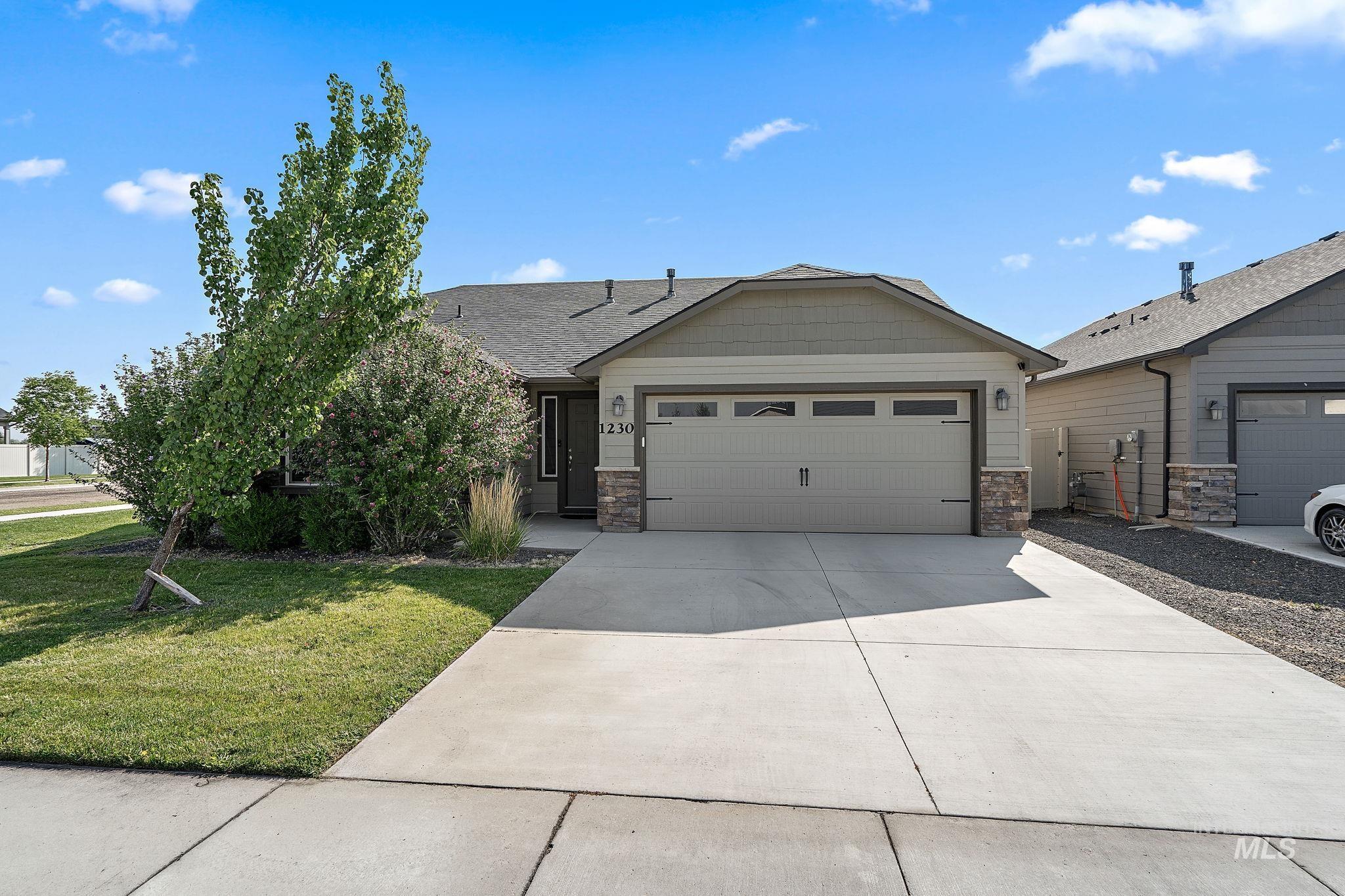 Ranch-style house featuring an attached garage, driveway, stone siding, a front yard, and roof with shingles