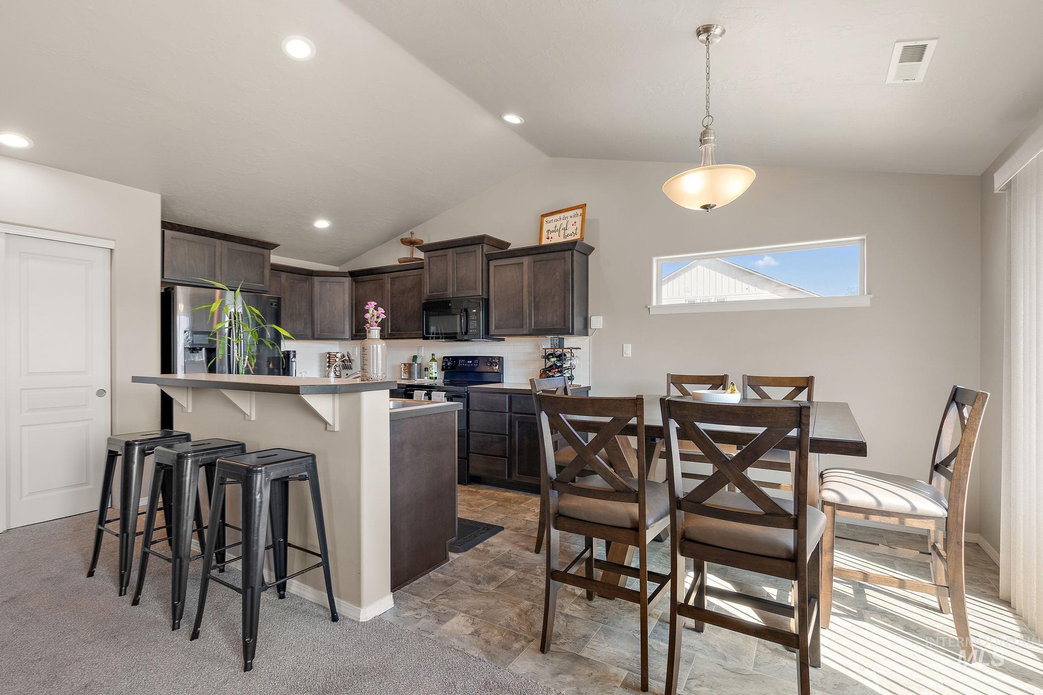 Kitchen featuring dark brown cabinetry, a kitchen breakfast bar, black appliances, vaulted ceiling, and light countertops