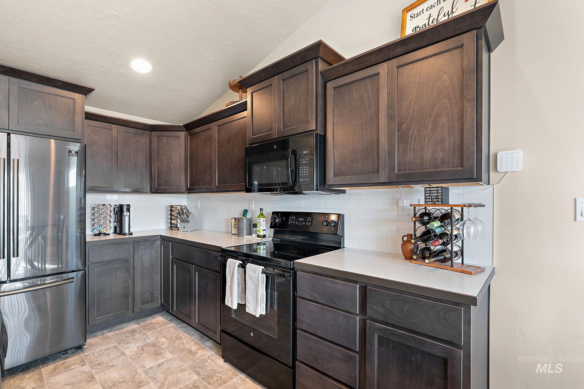 Kitchen featuring black appliances, dark brown cabinets, backsplash, lofted ceiling, and light countertops