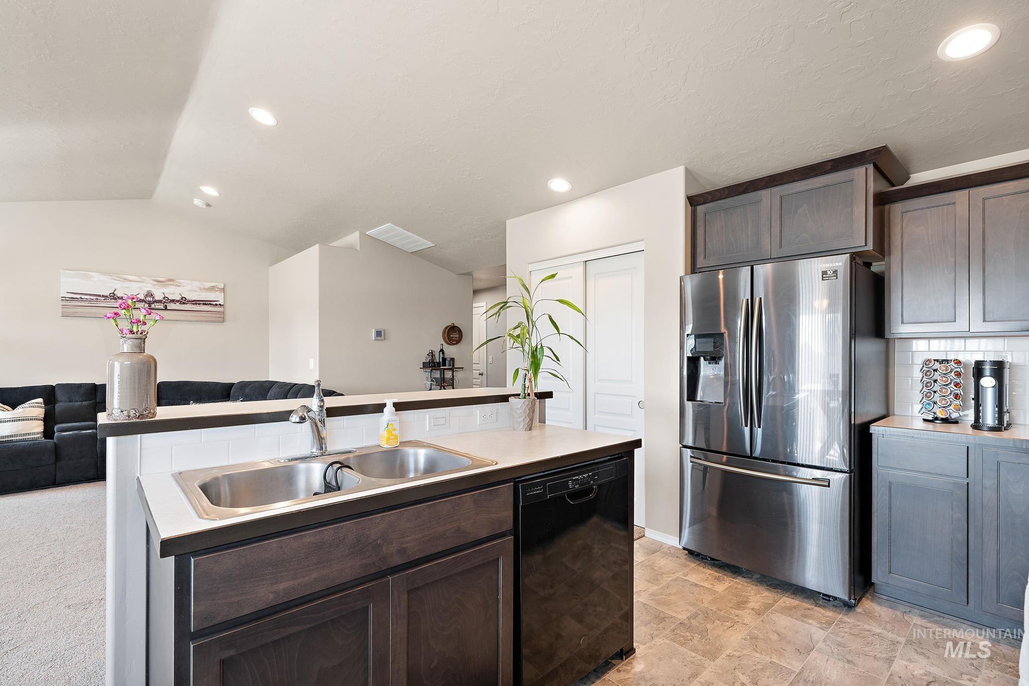 Kitchen with dark brown cabinetry, stainless steel fridge with ice dispenser, open floor plan, dishwasher, and a kitchen island with sink