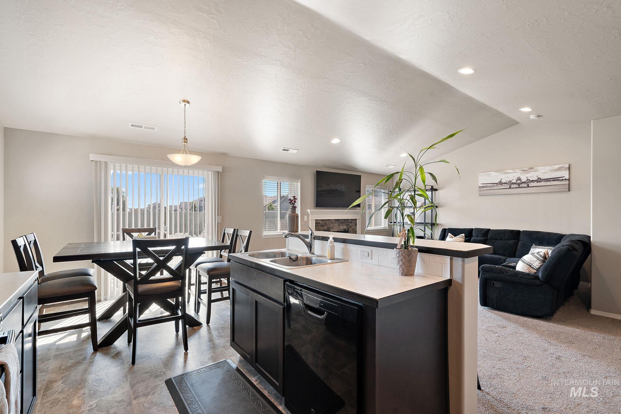 Kitchen with open floor plan, a textured ceiling, dark cabinetry, an island with sink, and black dishwasher