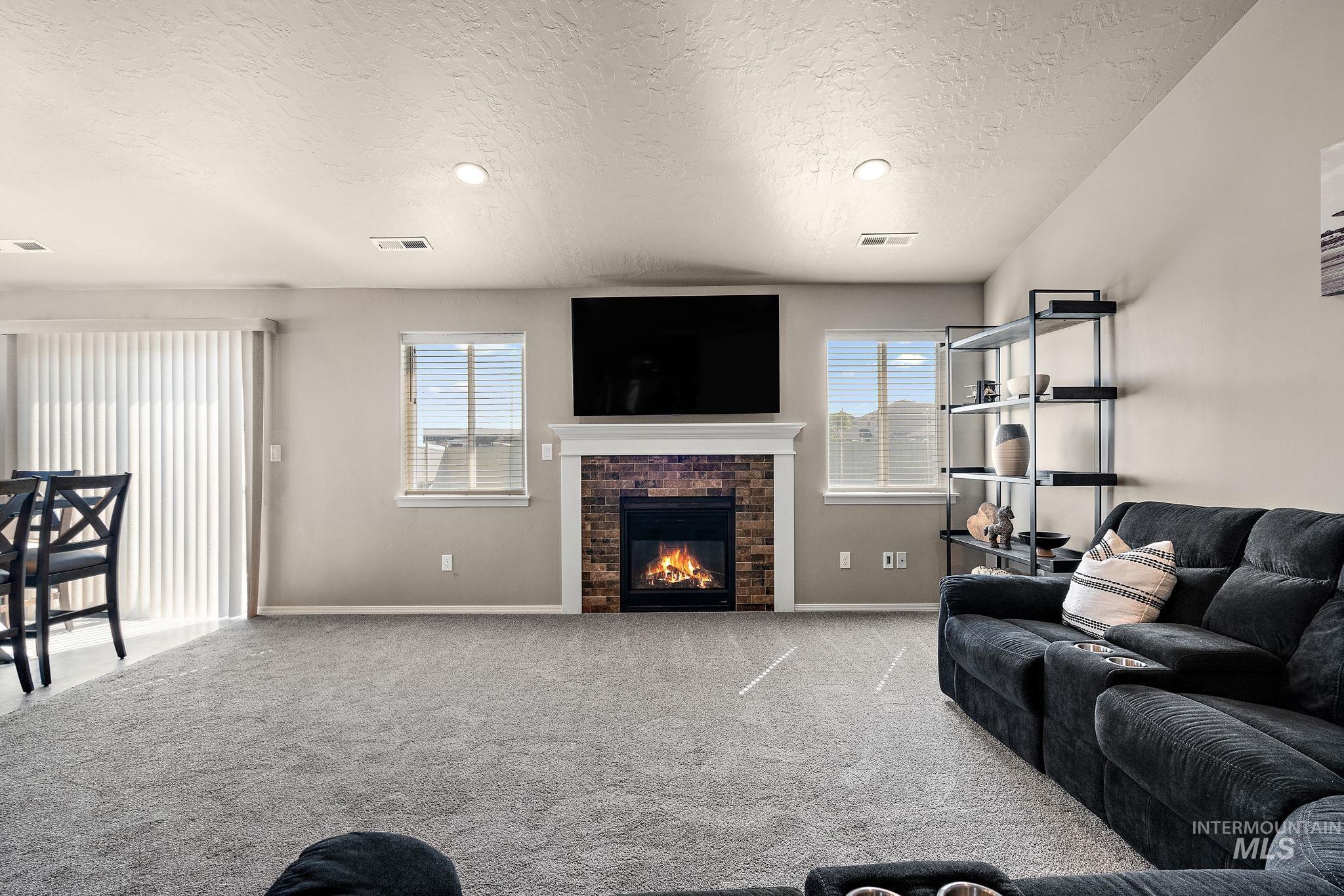 Carpeted living room featuring a brick fireplace and a textured ceiling