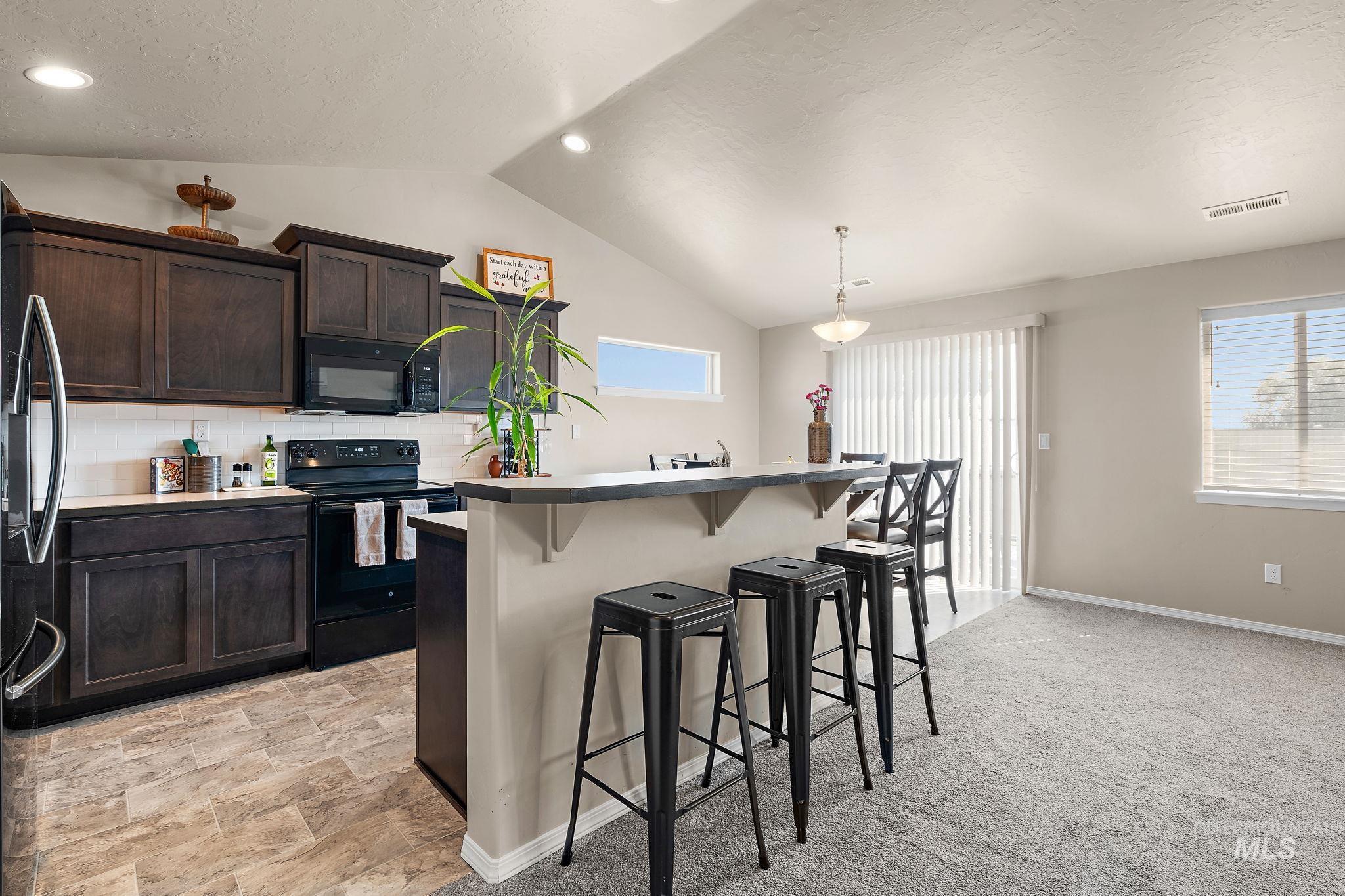 Kitchen with a kitchen bar, black appliances, decorative backsplash, a textured ceiling, and vaulted ceiling