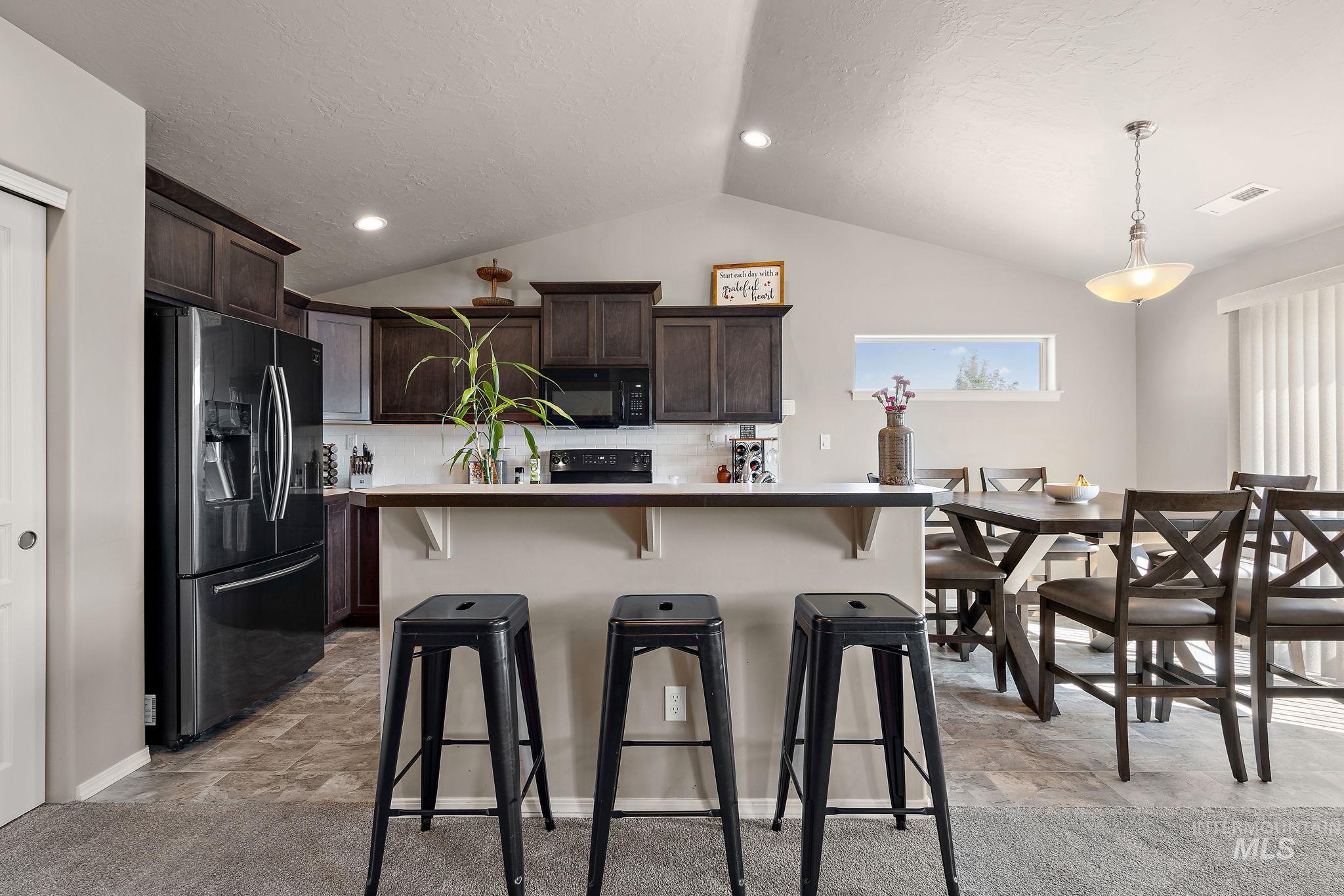 Kitchen featuring dark brown cabinets, black appliances, tasteful backsplash, a kitchen bar, and lofted ceiling