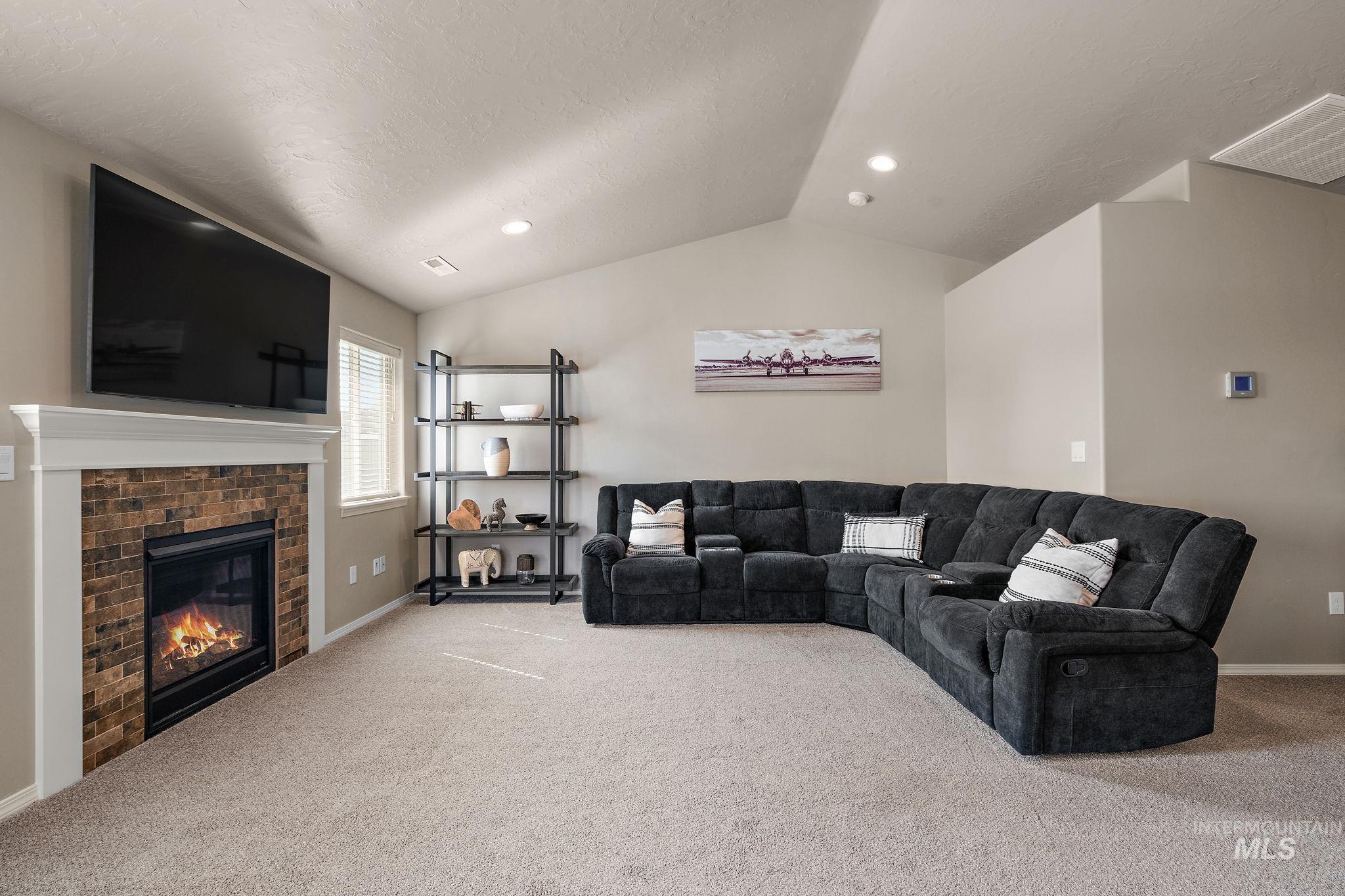 Carpeted living area with vaulted ceiling, a fireplace, a textured ceiling, and recessed lighting