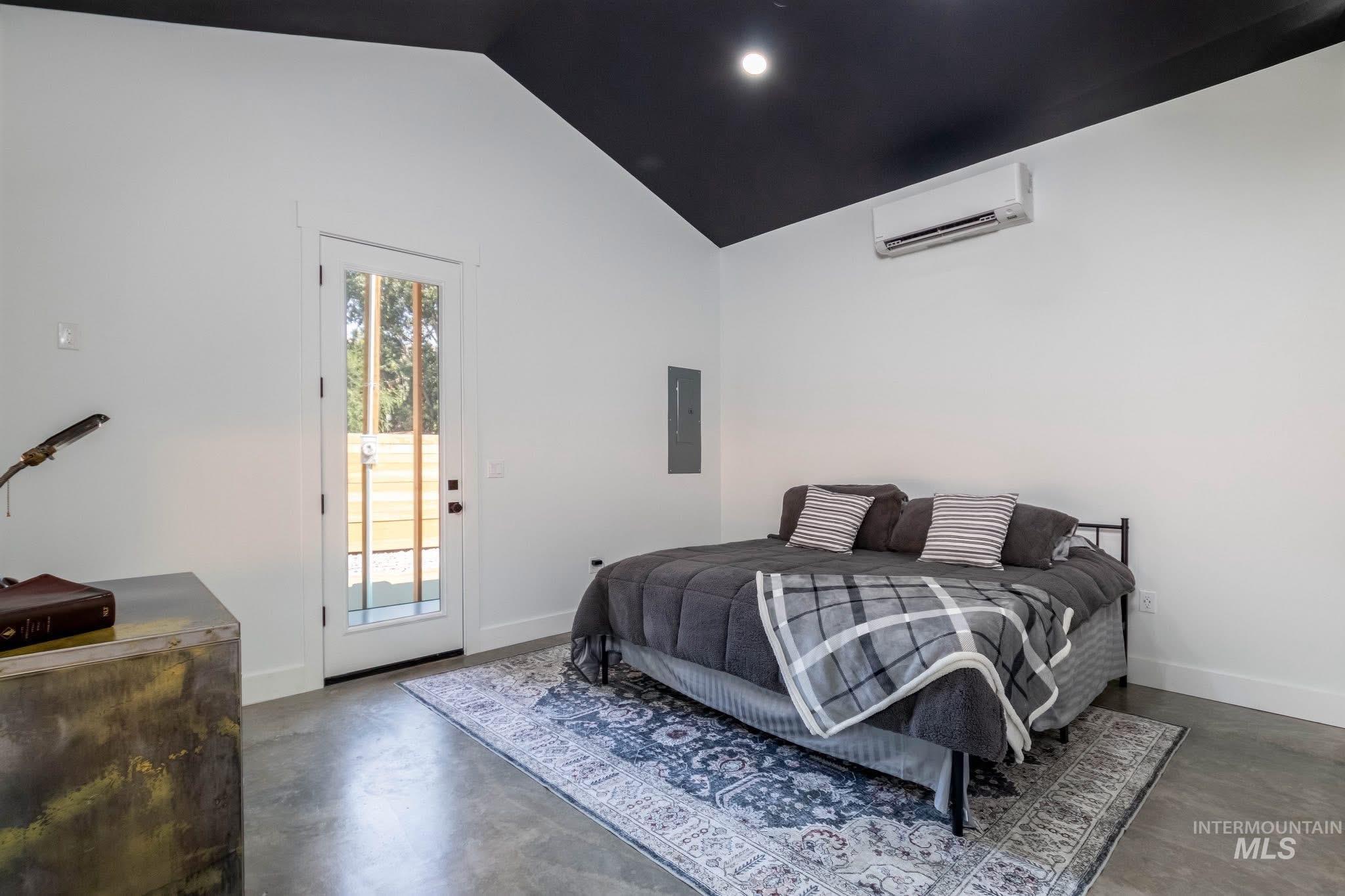 Bedroom with finished concrete floors, access to outside, lofted ceiling, electric panel, and recessed lighting