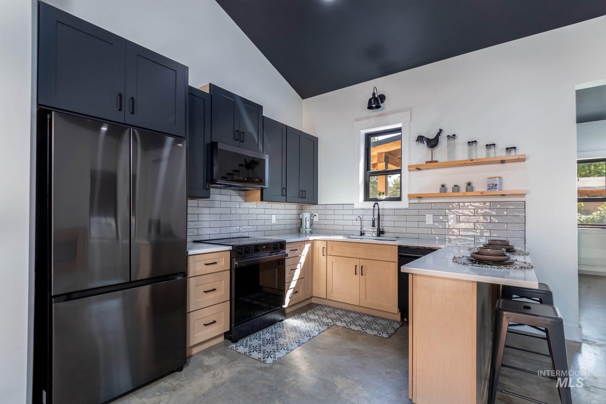 Kitchen with black appliances, a peninsula, backsplash, vaulted ceiling, and a kitchen bar