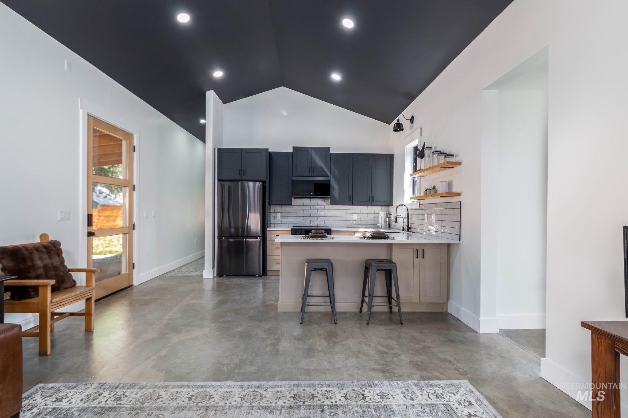 Kitchen featuring a kitchen breakfast bar, tasteful backsplash, freestanding refrigerator, a peninsula, and concrete floors