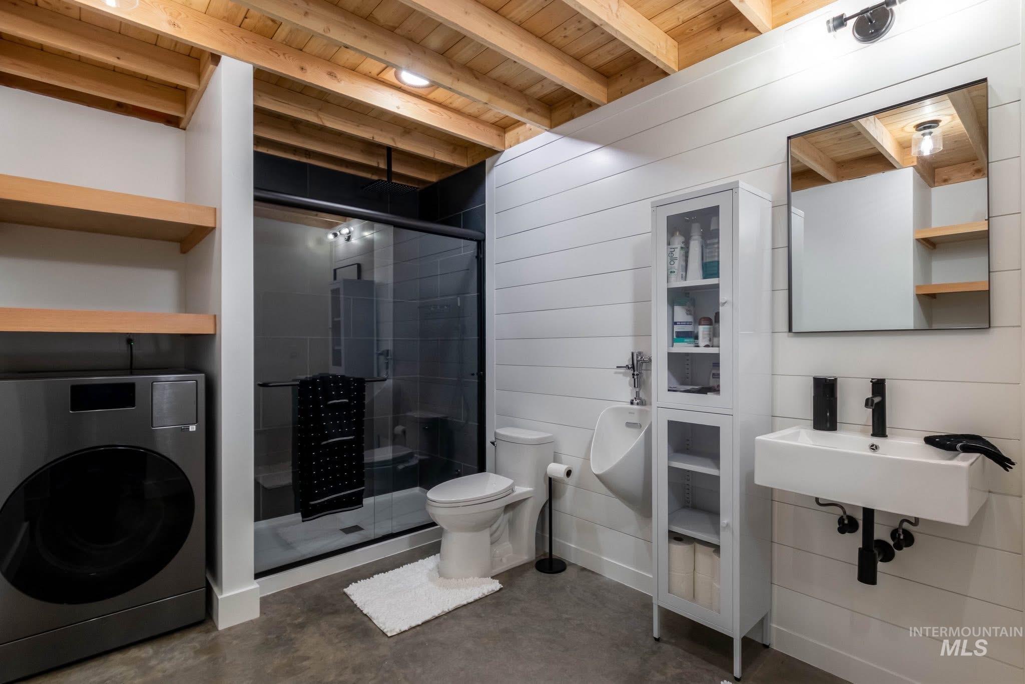 Bathroom featuring washer / dryer, a wooden ceiling with exposed beams, a shower stall, and concrete floors