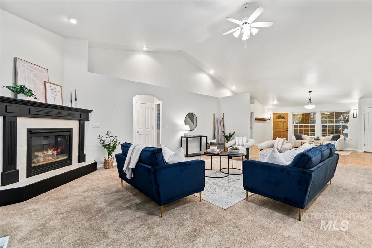 Living area featuring lofted ceiling, a glass covered fireplace, arched walkways, light carpet, and ceiling fan