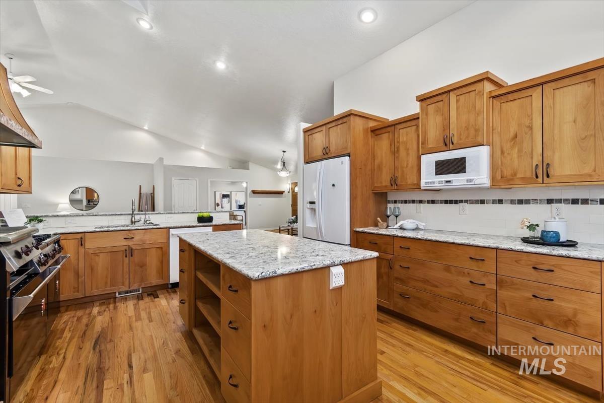 Kitchen with lofted ceiling, brown cabinetry, tasteful backsplash, open shelves, and light wood-type flooring