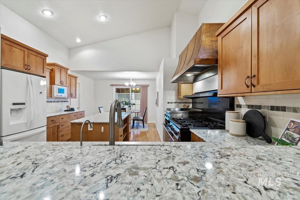 Kitchen featuring white appliances, brown cabinets, tasteful backsplash, light stone counters, and recessed lighting
