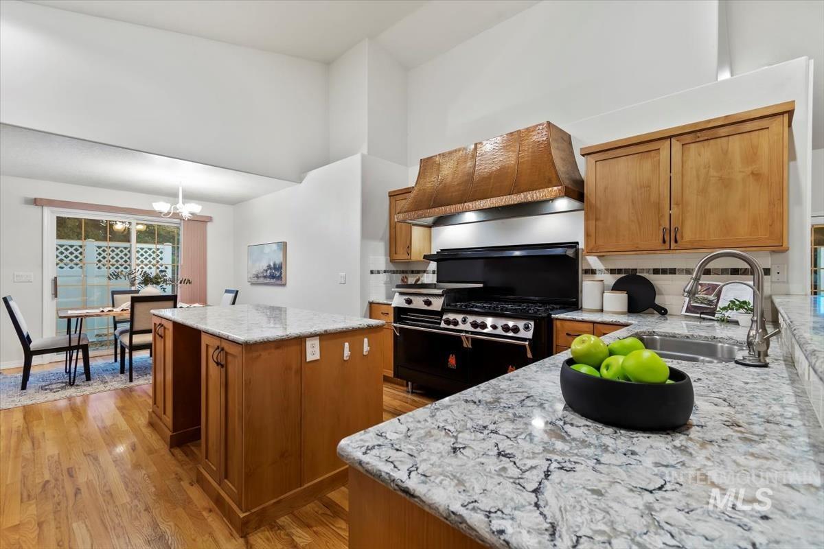 Kitchen with brown cabinets, tasteful backsplash, light stone countertops, custom exhaust hood, and light wood-type flooring