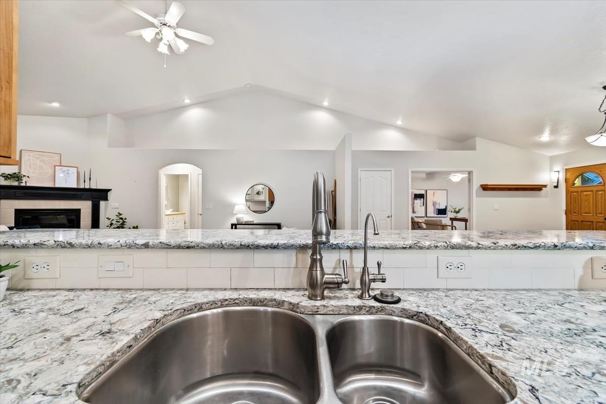 Kitchen view of a ceiling fan, light stone countertops, a glass covered fireplace, and recessed lighting