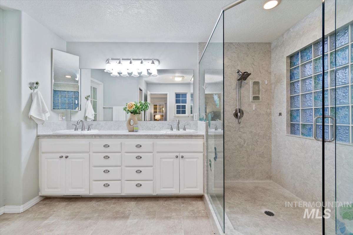 Full bath with a stall shower, double vanity, a textured ceiling, and light tile patterned floors