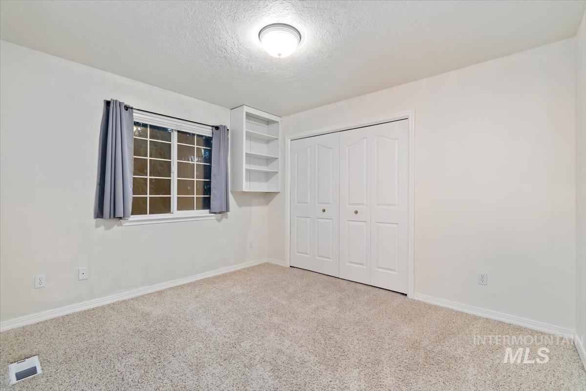 Unfurnished bedroom featuring light colored carpet, a textured ceiling, and a closet