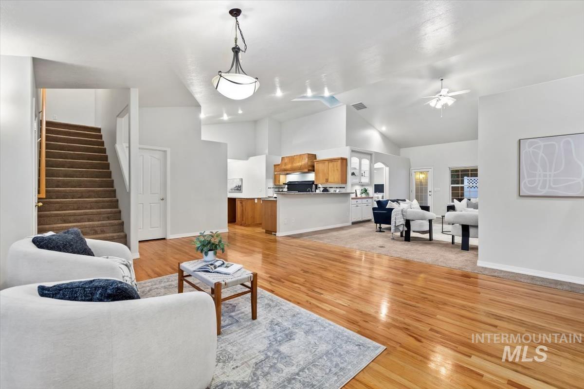 Living room featuring light wood finished floors, stairway, a ceiling fan, and high vaulted ceiling