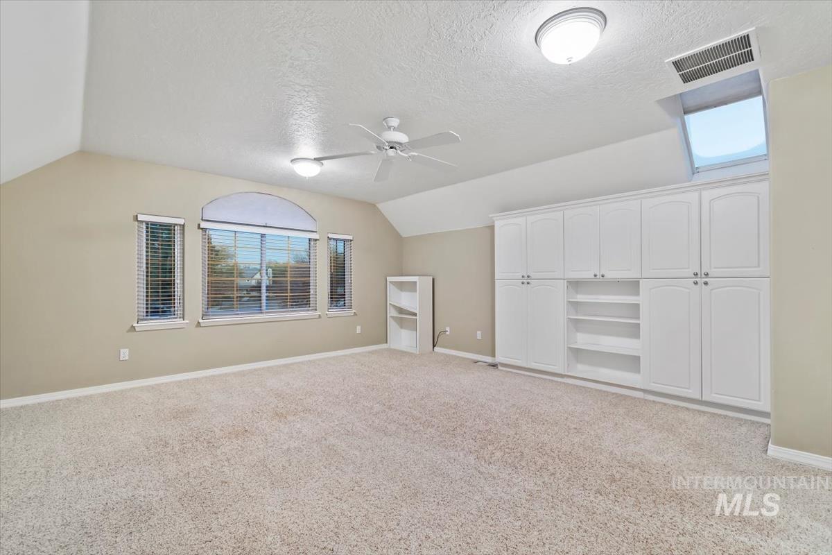 Additional living space featuring healthy amount of natural light, vaulted ceiling, light carpet, a textured ceiling, and ceiling fan