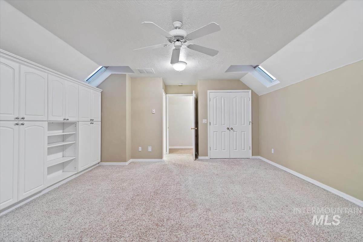 Bonus room with lofted ceiling, a skylight, a textured ceiling, light carpet, and ceiling fan